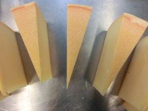 Vier Stücke Käse, jeweils in vier kleinere Stücke geschnitten, liegen auf einem Holzbrett.